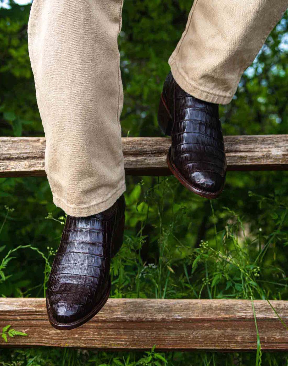 Man sitting on fence wearing a pair of RUJO black caiman cowboy boots