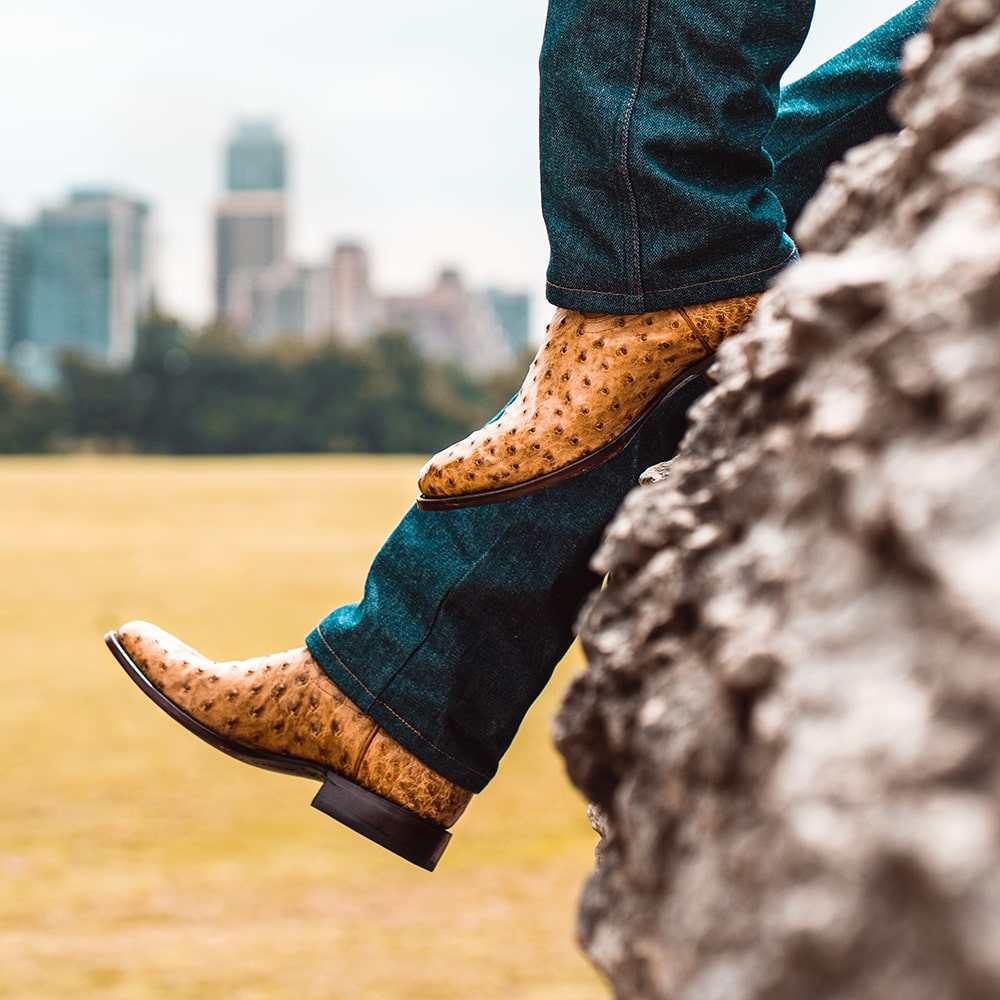 Man wearing RUJO Full-Quill Ostrich cowboy boots resting on rock