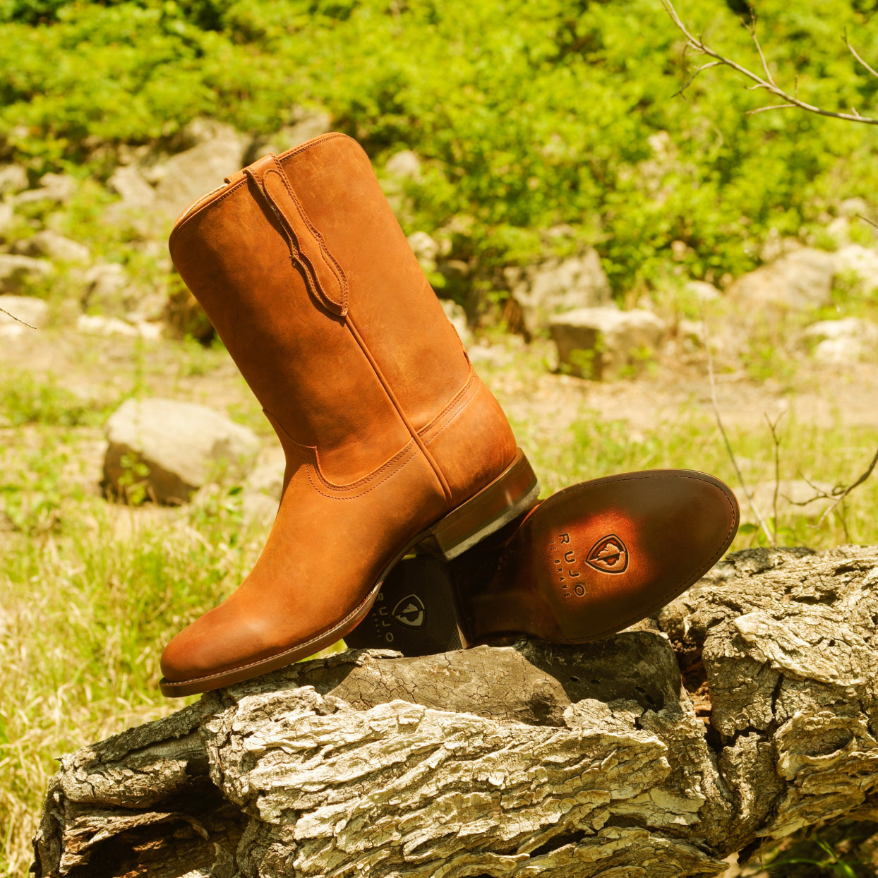 A pair of RUJO Rock Ranch Calfskin cowboy boots set on a rock in a prairie