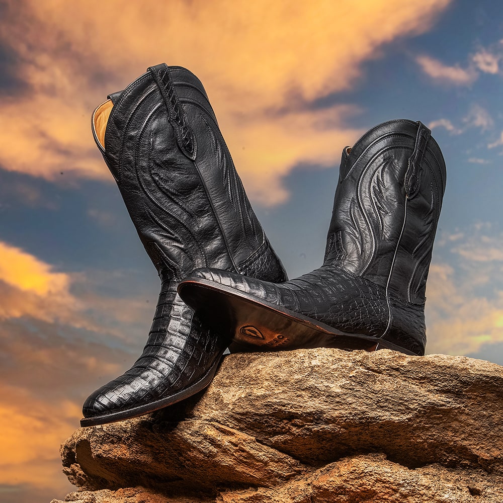 A pair of RUJO Caiman cowboy boots sitting on a rock at sunset