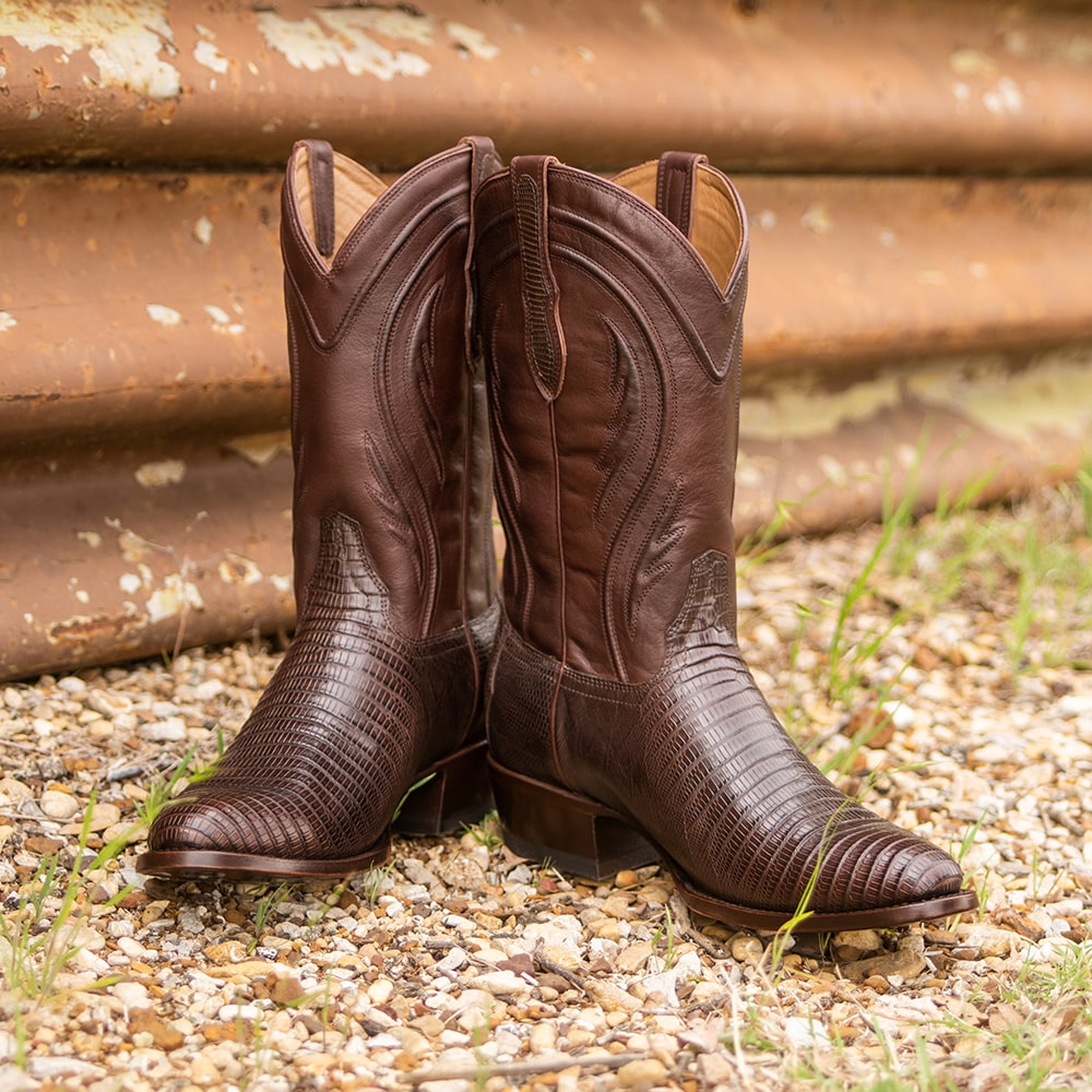 A pair of brown RUJO Teju Lizard cowboy boots sitting on gravel