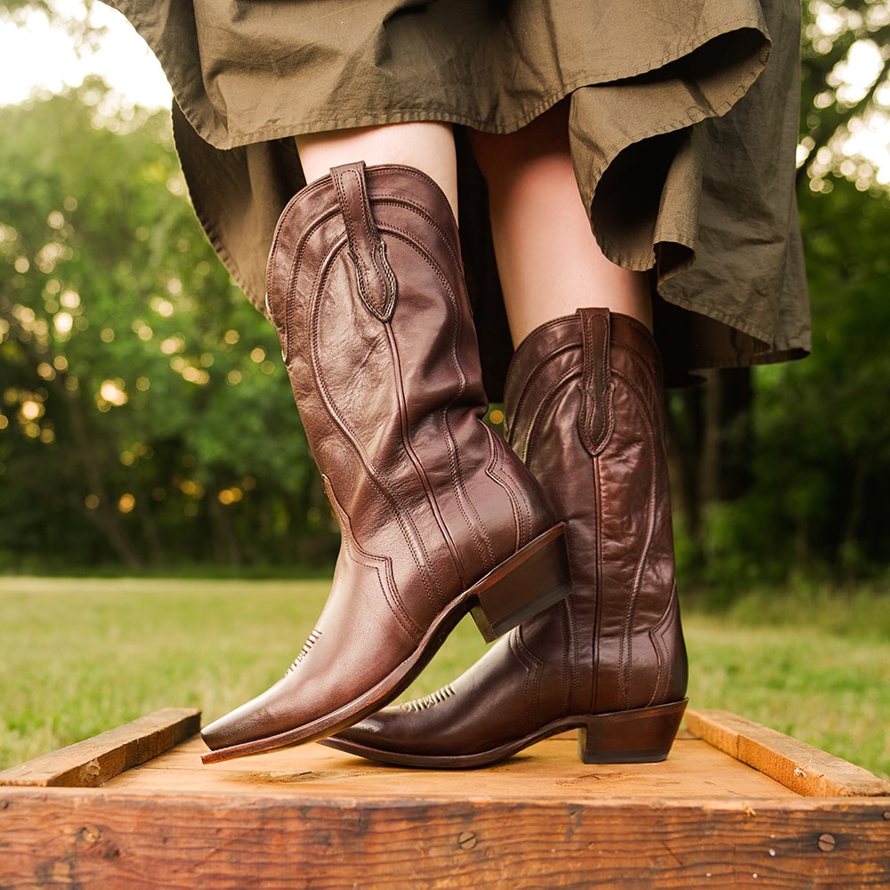 Woman in green dress standing on box wearing RUJO cowgirl boots