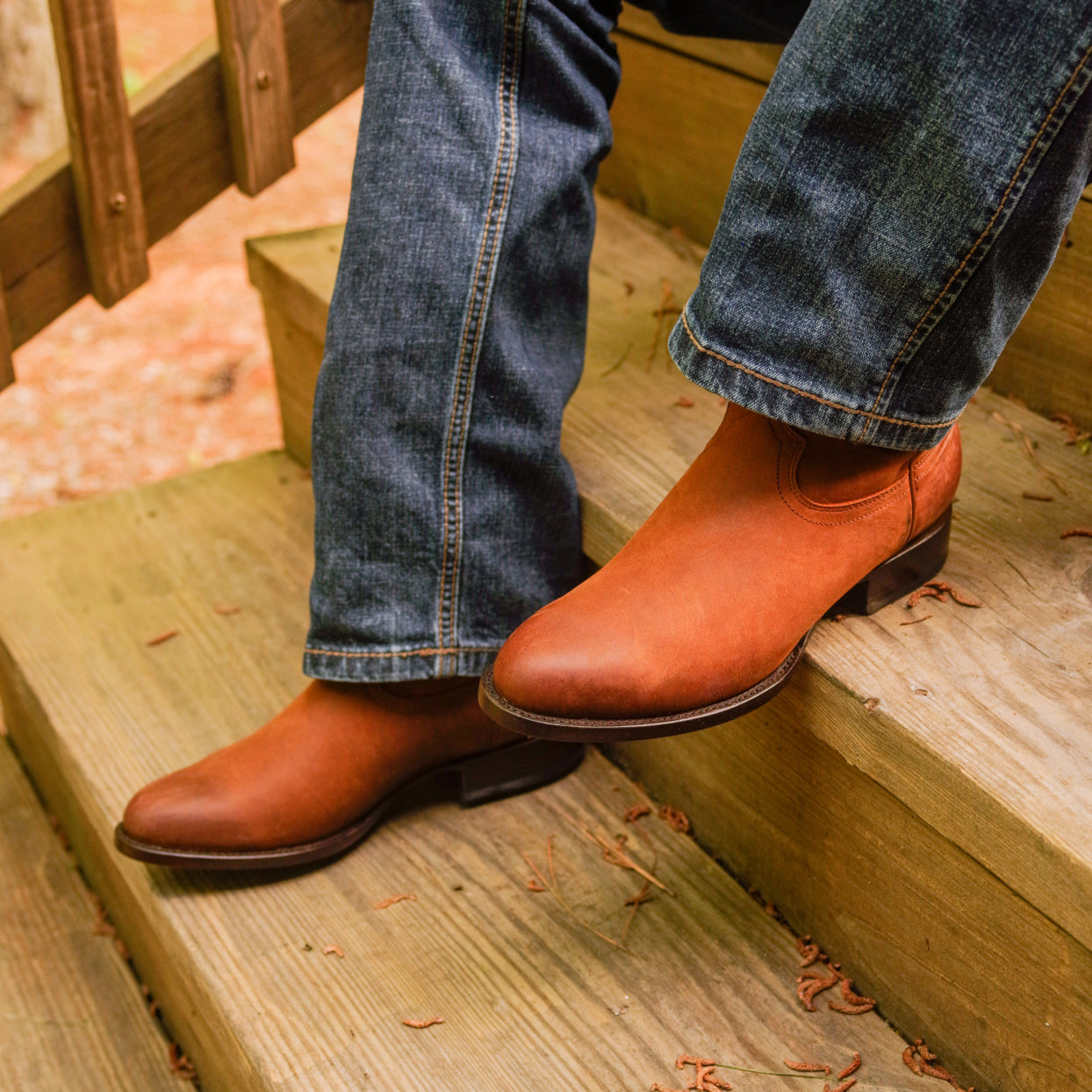 Man sitting on wooden steps wearing a pair of RUJO Rock Ranch Calfskin cowboy boots