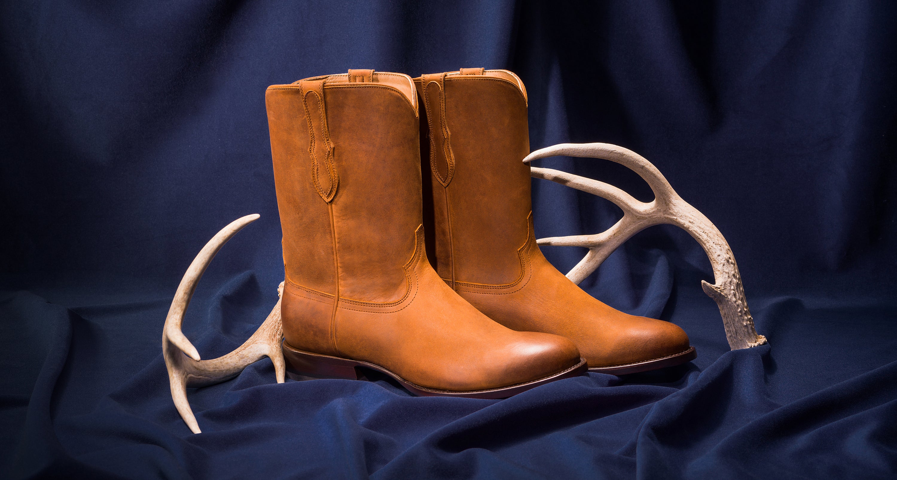 A pair of men's RUJO calfskin cowboy boots set next to a pair of antlers