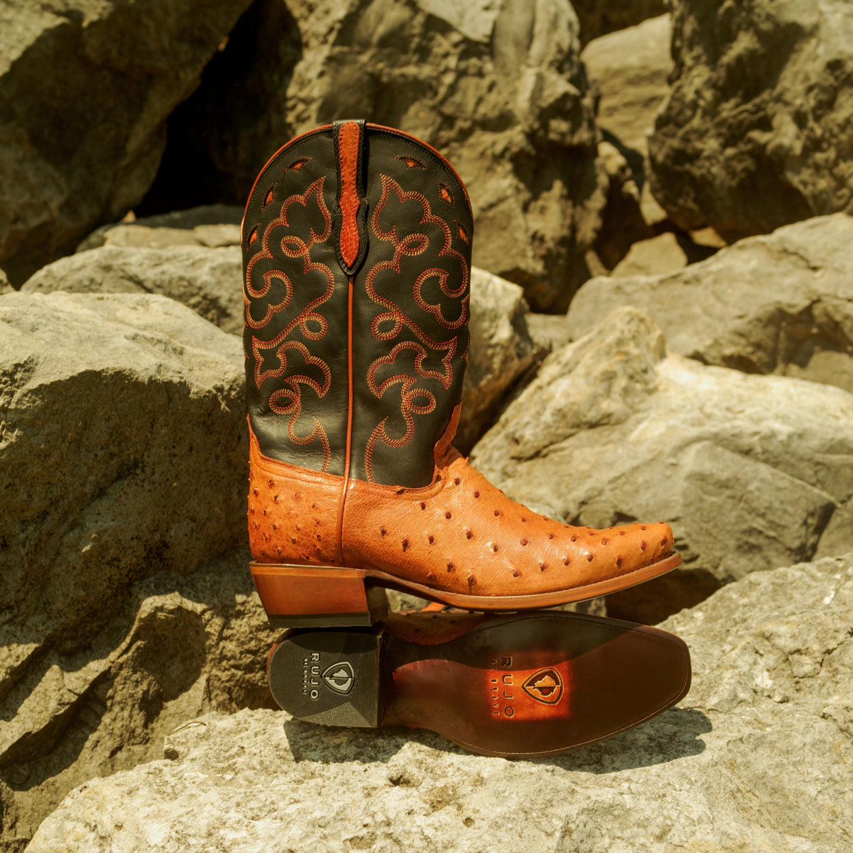 A pair of RUJO Full-Quill Ostrich cowboy boots set up on some rocks