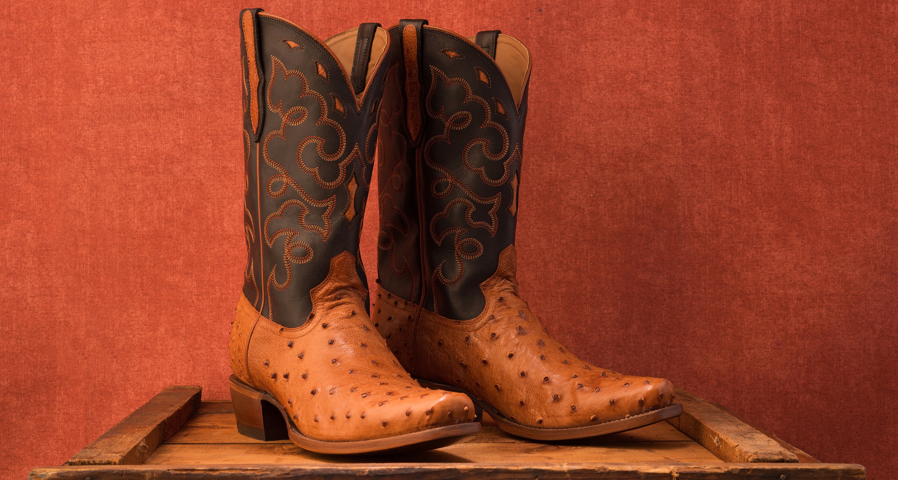 A pair of RUJO full-quill ostrich cowboy boots set on a wooden crate