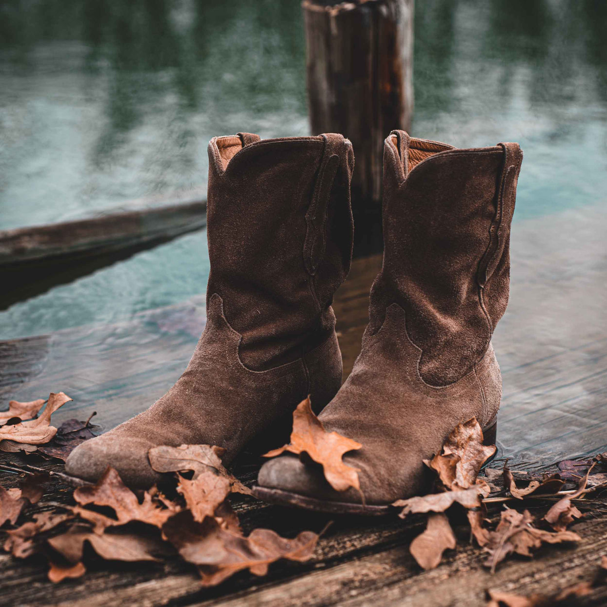 A pair of RUJO Sentry Suede cowboy boots sitting on a dock next to water