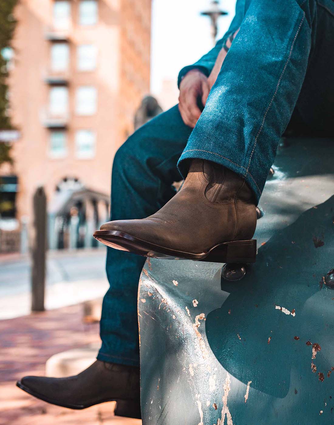 Man sitting on the hood of a truck wearing brown square-toe cowboy boots.